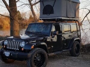 Tienda de techo Sprint en una camioneta negra Jeep, mostrada en un bosque con un lago en un día de otoño.