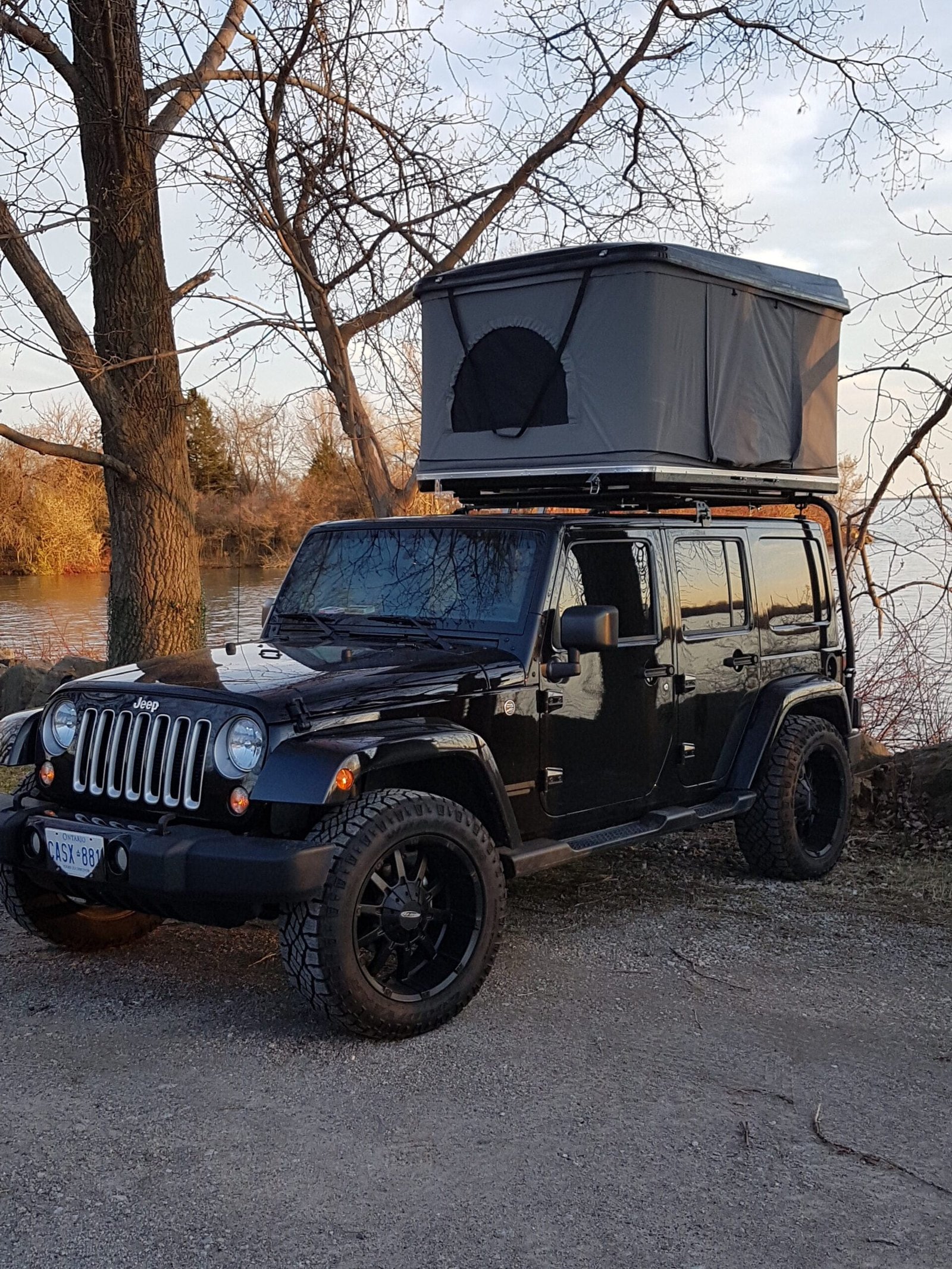 Tienda de techo Sprint en una camioneta negra Jeep, mostrada en un bosque con un lago en un día de otoño.