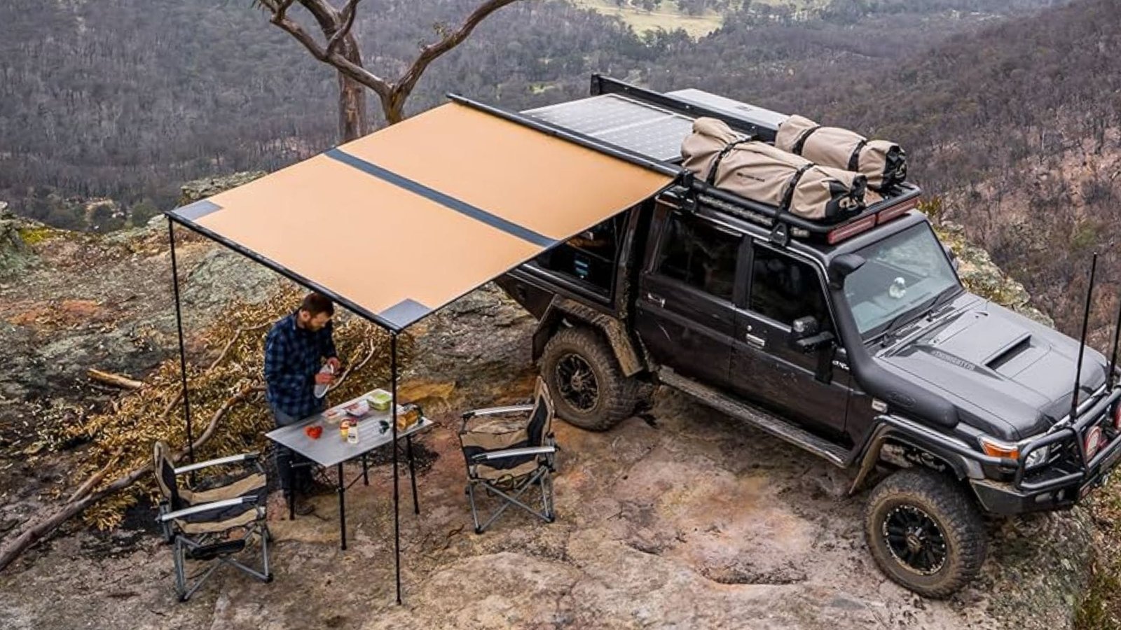 Camioneta negra con toldo instalado y persona disfrutando el dia debajo del toldo en una montaña