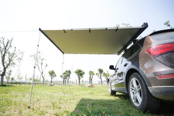 Camioneta estacionada en un campo con el toldo enrollable de aluminio desplegado en su lateral.